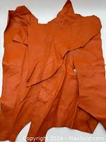 Five irregular pieces of orange leather laid out folded, showing smooth leather texture, measuring roughly 20x20 inches total.
