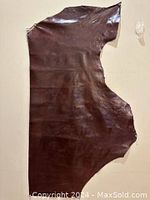 Full view of the irregular red brown leather piece showing its shape and glossy surface.