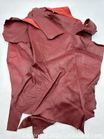 Three irregular pieces of red leather with smooth texture on front.