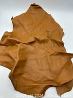 Full view of two irregular pieces of saddle brown leather showing texture and size