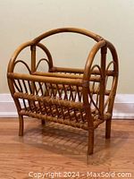 Front and side view of honey-coloured rattan magazine rack with vertical slats and rounded top handles, showing heart cutout detail on the sides and woven rattan base.