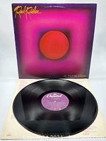 Vinyl record disc with purple Capitol Records label, placed facing upward on top of album cover. Album cover has a purple-pink gradient background with a large red circle center and yellow 'Red Rider' text at top left.