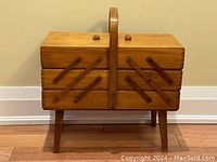 Closed view of vintage wooden sewing basket showing legs, handle, wooden finish, and compact form.