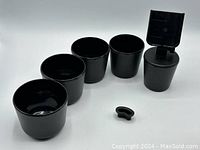 Photo of five black plastic interchangeable base cups arranged in size order with small detachable component in front on a white background.