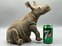 Overall view of the baby white rhino statue sitting next to a 7-up can for scale, showing detailed texture and size.