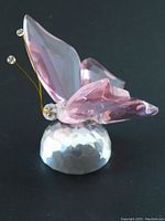 Side view of the pink winged crystal butterfly sitting on the faceted clear glass base showing wire antennae and wing detail.