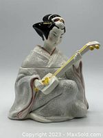 Front and side view of the ceramic Geisha figurine playing the shamisen with detailed textured kimono and painted hair ornaments.