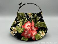 Front view of small cotton barkcloth fabric purse with tropical hibiscus and plumeria flower design on black background, with metal kiss lock frame and handle.
