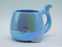 Side view showing the smiling eye with eyelashes, pink cheek, fin at base, and tail forming handle with iridescent blue ceramic.