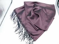 Folded dark mauve pashmina shawl with black fringe laid flat on white surface