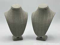 Two gray fabric jewellery display bust stands positioned side by side on a plain background, showing front and side profile.