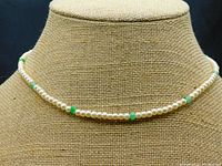 Front view of pearl necklace on tan display bust showing cream pearls and interspersed green jade beads.
