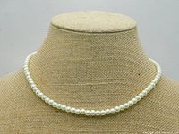 Full view of the pearl necklace displayed on a fabric bust showing the single strand of cream-colored pearls.