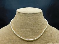 Front view of the pearl necklace displayed on neutral-textured bust.