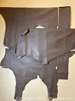 Four irregular grey leather hides overlapping on a beige background, showing overall size and shape.
