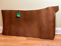 Front view of large, irregular shaped thick leather sheet in red brown color against wall on wood floor.