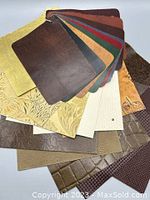 Leather sample swatches in multiple colors, some smooth and some textured with patterns and embossing.