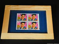 Block of four unused 29 cent Elvis Presley stamps in natural pine wood frame on navy blue mat under glass, shown against black background.