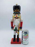 Front view of vintage Kingsbridge wooden nutcracker with a Canada Dry Diet Ginger Ale can for size comparison, showing detailed hand painted features and faux fur beard.