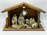 Vintage nativity scene inside wooden manger with seven resin figures and a silver star mounted on the back wall.