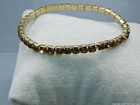 Full view of the vintage topaz rhinestone tennis bracelet laid in a circular shape showing the gold-tone expansion band and continuous row of stones.