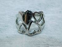 Connected heart ring front view showing one solid heart and three cut-out hearts in polished stainless steel.