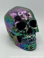 Angled side view of the iridescent skull showing purple, green, and gold tones.