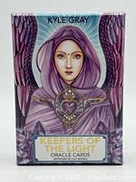 Front box artwork showing angelic figure with purple hood and wings, labeled 'KEEPERS OF THE LIGHT ORACLE CARDS ARTWORK BY LILY MOSES'