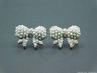 Close-up front view of the pair of silver-tone bow stud earrings with faux seed pearls and rhinestone center accents.