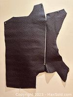 Two irregular pieces of black leather with ostrich pattern, laid flat with pins for scale and to maintain shape.