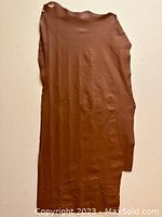 Full view of the irregular shaped medium brown leather piece hanging vertically showing the overall size and shape.