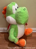 Side profile shot of the large 36-inch Yoshi plush toy showing the green and white body, orange feet, and back features