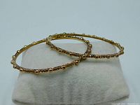 Two yellow gold tone vintage bangle bracelets displayed on a white cushion, showing the circular shape and gold balls alternating with topaz-colored stones.