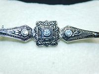 Close-up of the front side center segment of the brooch showing clear stones and detailed engraved pattern in silver tone metal.