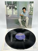 Vinyl record cover front featuring Lionel Richie sitting on a chair in a light room, with the record partially visible below it showing the label.