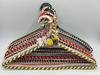 Twelve vintage wire hangers wrapped in colorful braided and twisted fabric strips stacked horizontally showing overall lot.
