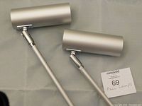 Pair of brushed aluminum cylindrical lamps laid out side by side showing the adjustable swivel heads and matte silver finish.