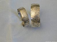 Two sterling silver cuff bracelets displayed side by side showing floral engravings and size difference.