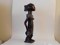 Side view of the tall wooden sculpture showing the slender torso, carved detailing and polished surface.