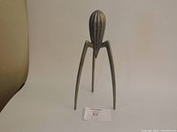 Front view of aluminum citrus juicer standing on three curved legs