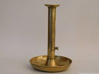 Front view of antique brass push-up candle holder showing round dish base and tall cylindrical stem.