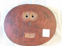 Front view of Baule Goli Kple Kple mask. Large oval shape painted red with carved eyes and mouth.