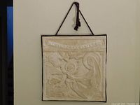 Full front view of relief plaque with hanging cord visible