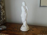 Front view of statue on wood surface showing overall shape and drapery details