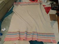 Full view of the Hudson's Bay blanket spread out showing the cream fabric with stripes of peach, light blue, yellow, and green along the bottom edge.