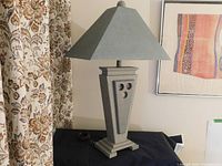 Photo of the full lamp showing geometric design base, custom painted gray shade, and fabric curtain background.