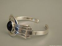 Side angle view of silver cuff bracelet with black obsidian stone and stepped silver decorative design.