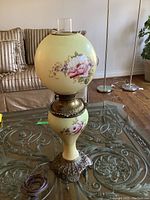 Full view of antique lamp with visible floral design and metal base, on glass table.