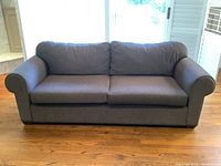 Front view of a brown fabric sofa with two seat cushions and two back cushions, sitting on wooden floor with window behind.