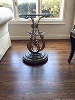 Full view of the end table showing iron base, stone circular platform, and clear glass top with natural light background.